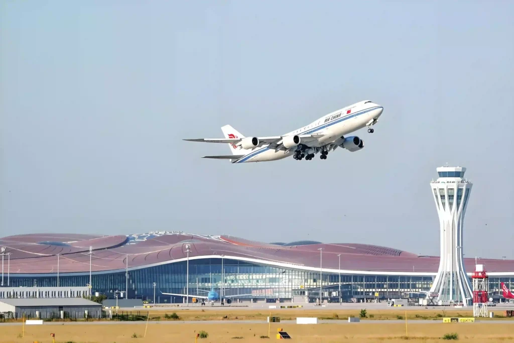 An Air China Boeing 747 climbing over the terminal and control tower at a modern Chinese airport