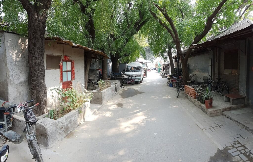 A tree-lined hutong alley in Nanluoguxiang, central Beijing, with grey brick courtyard houses