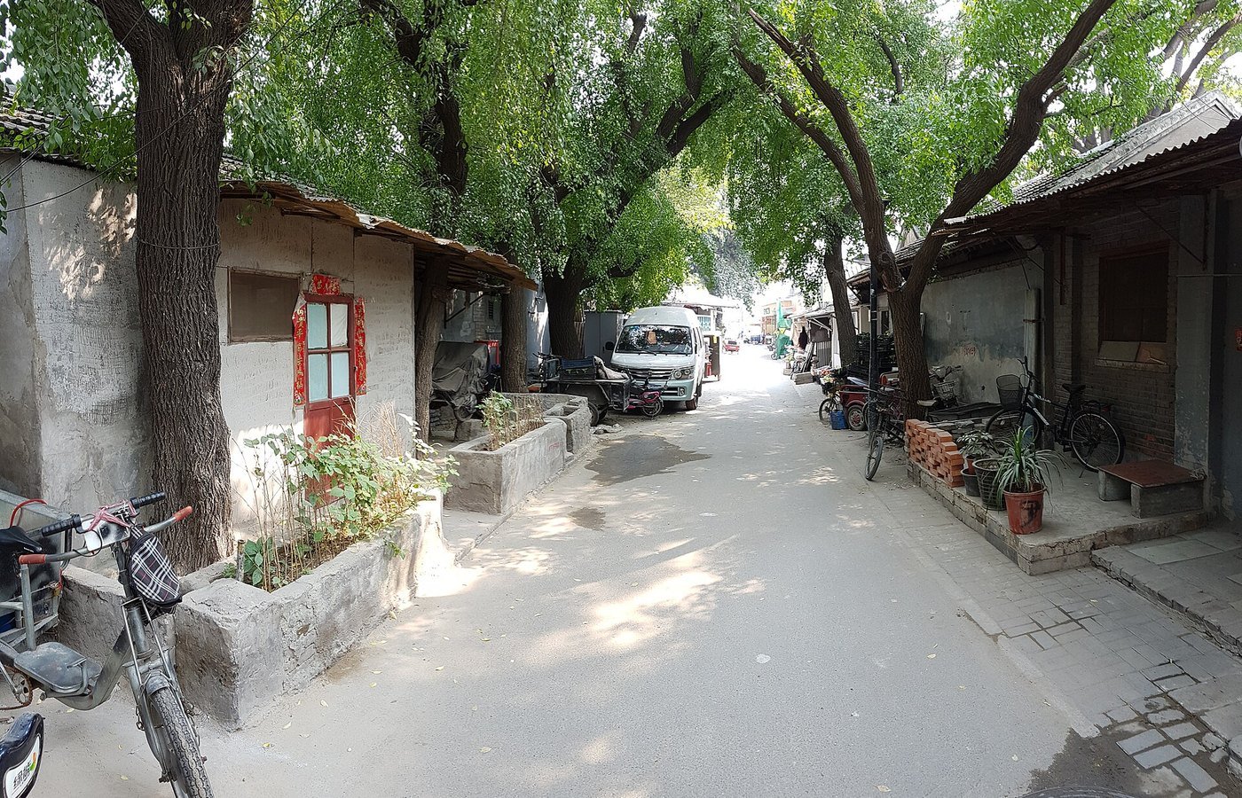 A tree-lined hutong alley in Nanluoguxiang, central Beijing, with grey brick courtyard houses