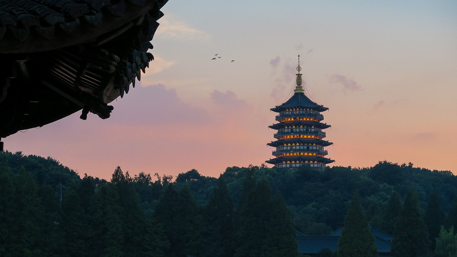 Leifeng Pagoda lit at dusk above the treeline on the south shore of West Lake in Hangzhou
