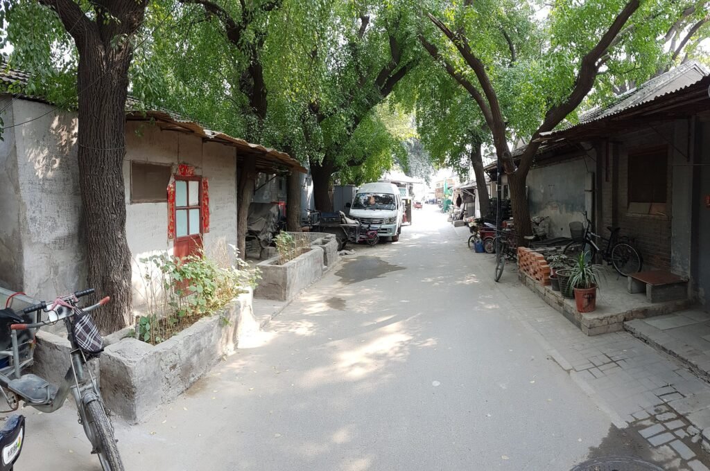 A tree-lined hutong alley in Nanluoguxiang, central Beijing, with bicycles and grey brick walls