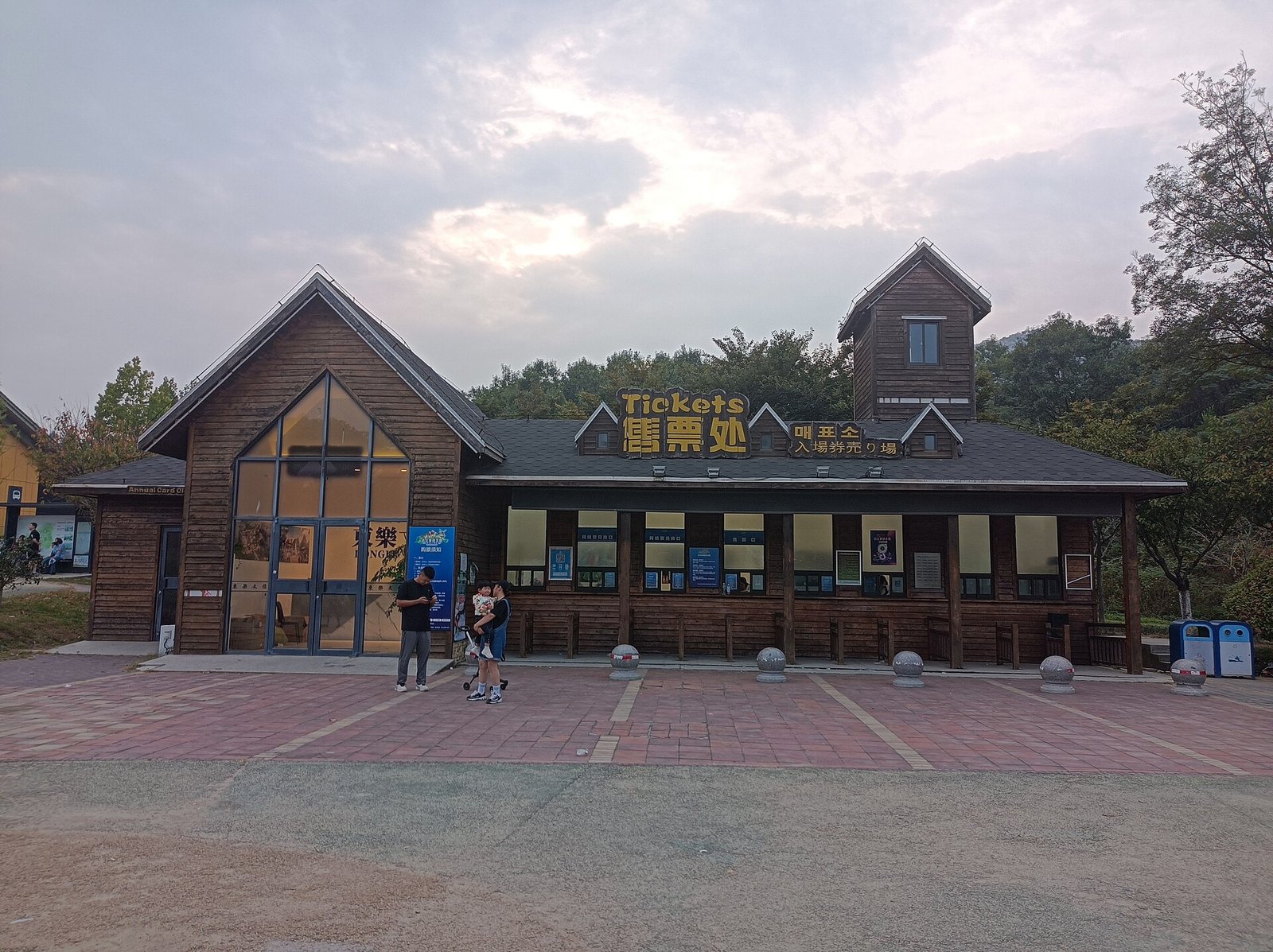 A wooden ticket office with a sign reading Tickets in English, Chinese and Korean, and a family walking towards it