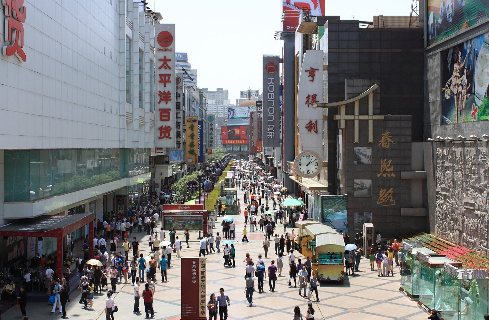 A crowded pedestrian shopping street in central Chengdu on a clear day, lined with shop signs and towers