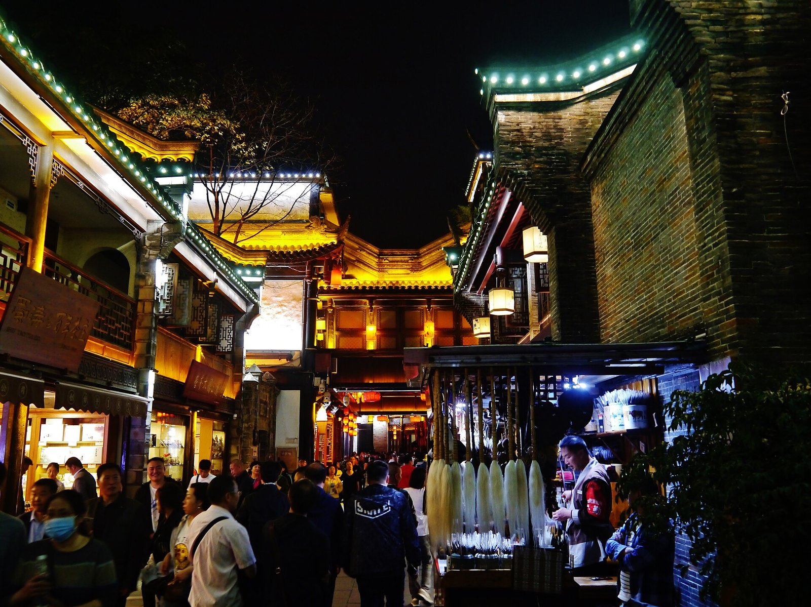 A lantern-lit old shopping street in a Chinese city at night, with red banners, snack stalls and crowds