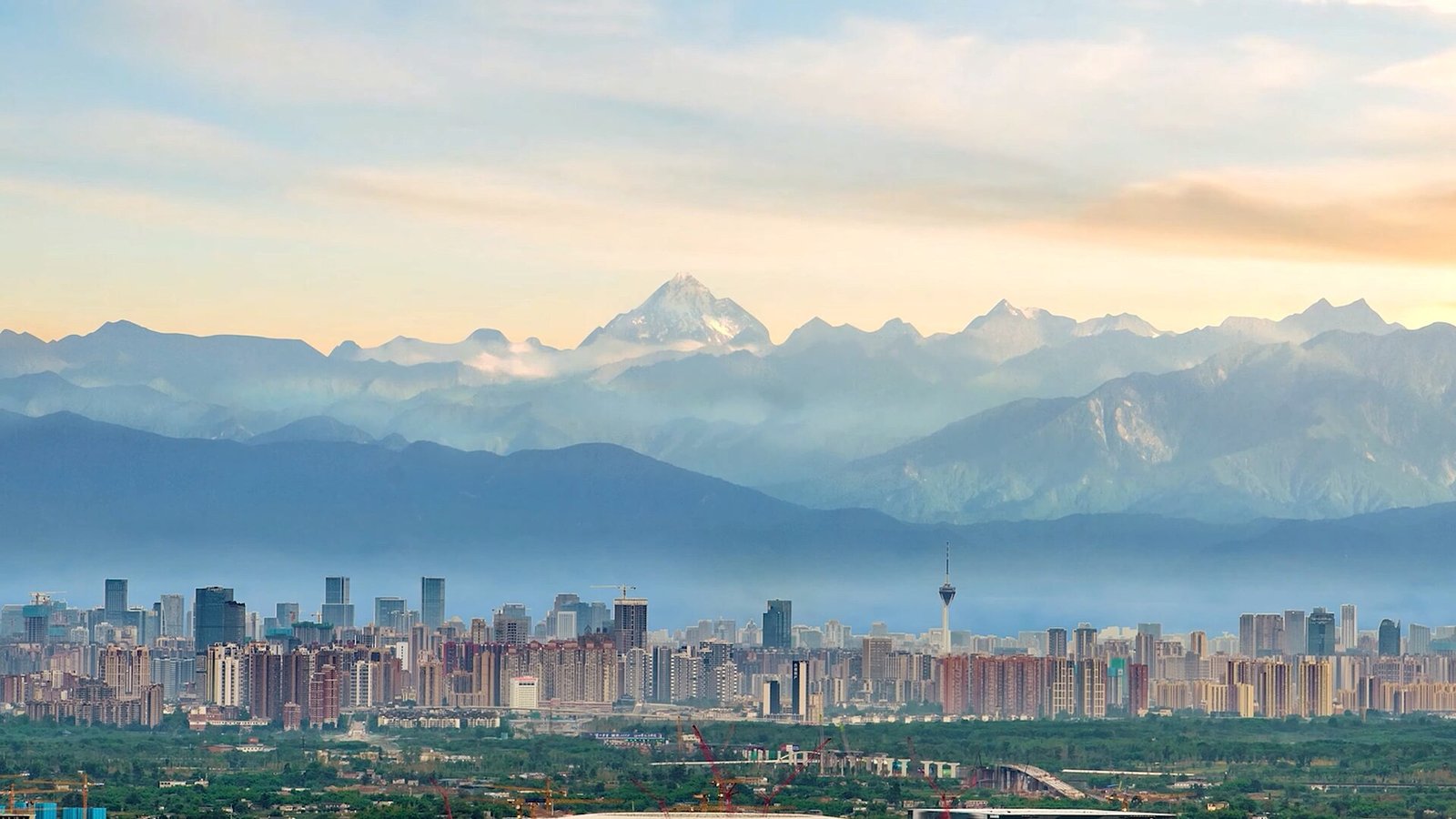 The Chengdu skyline at dusk with snow-capped mountains rising behind the city