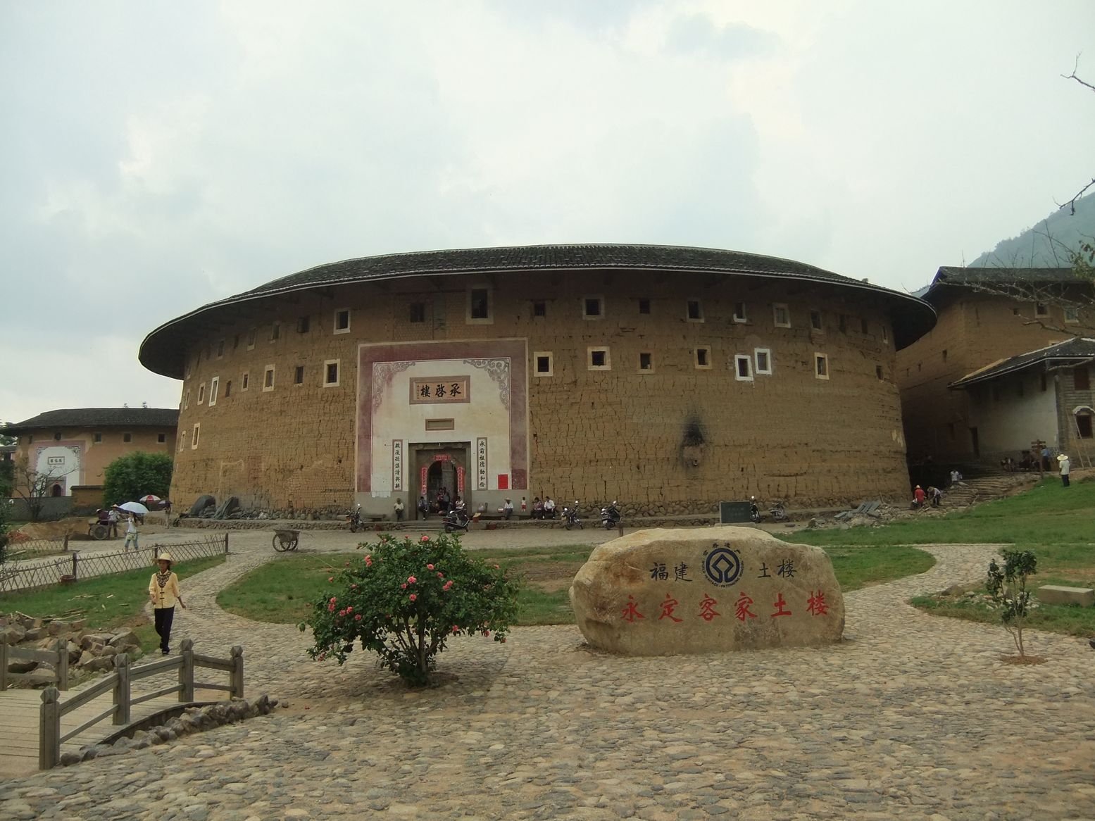 The broad circular earthen facade and arched entrance of Chengqi Lou in Yongding District, Longyan, with a stone marker in front