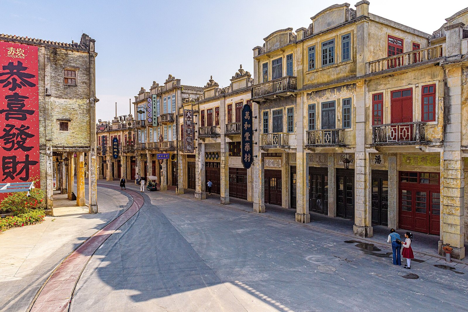 A wide restored street of arcaded shophouses with red lanterns and hanging signs, clean paving and no traffic