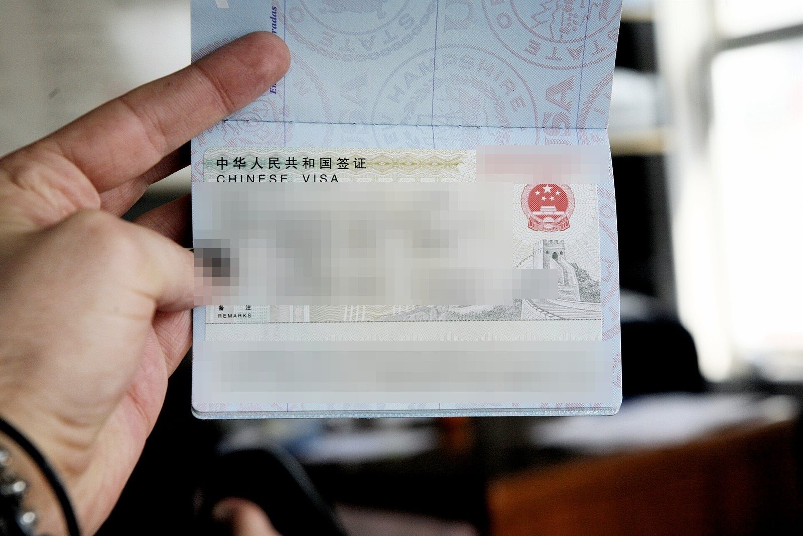 A Chinese L-category tourist visa sticker in a United States passport, with the personal details redacted