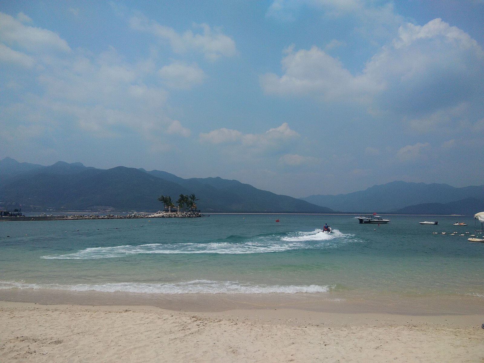 Surf breaking on a wide beach at Lingshui with green hills behind and an island offshore