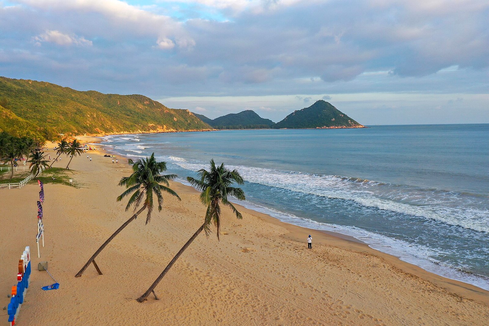 Palm trees leaning over white sand on Daidai Island in Lingshui, with two small islands offshore