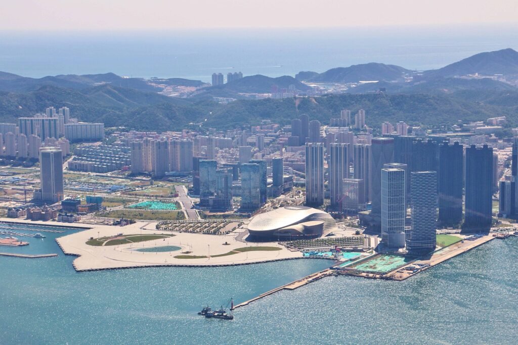 The Donggang waterfront in Dalian, a curved white convention centre on reclaimed land with high-rise towers behind