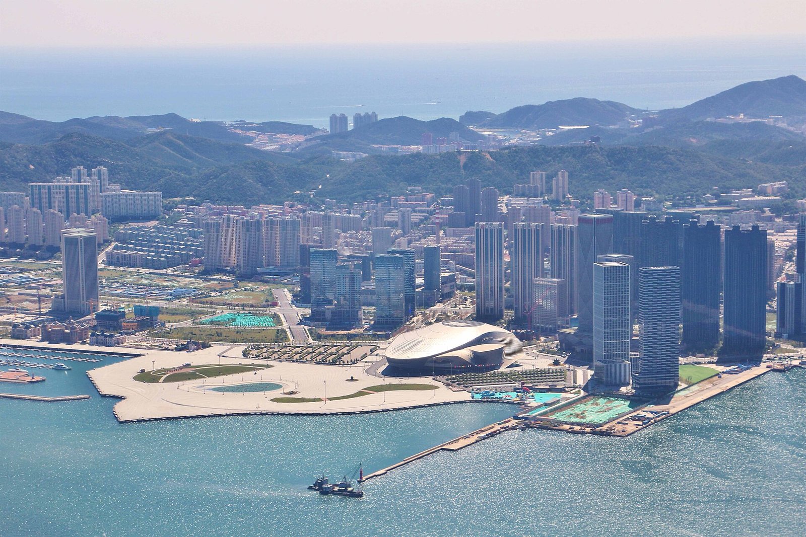 The Donggang waterfront in Dalian, a curved white convention centre on reclaimed land with high-rise towers behind