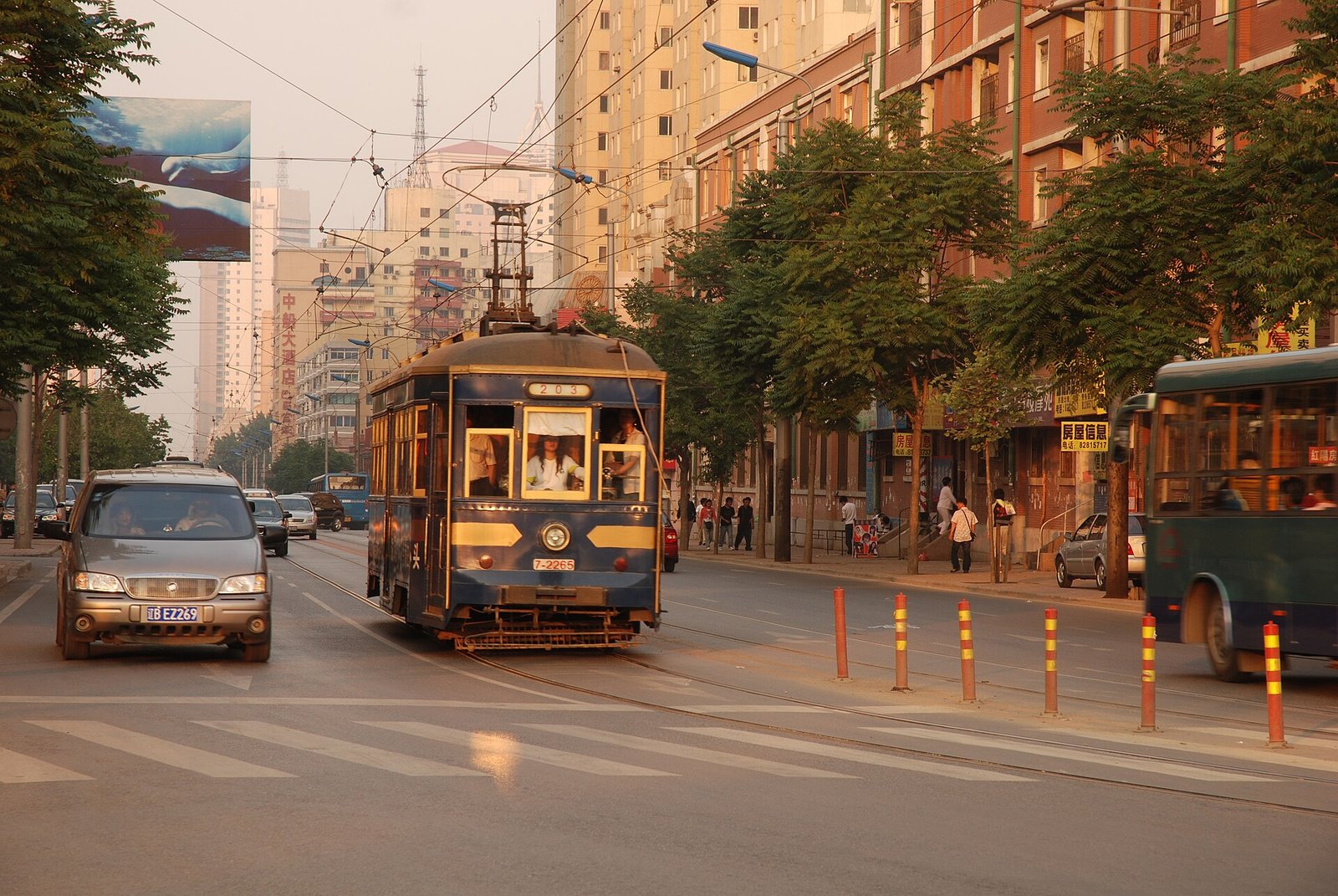 A vintage wooden-bodied tram running on a Dalian street, with colonial-era facades and modern traffic alongside