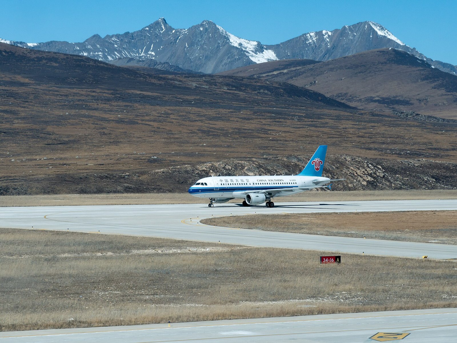 A passenger aircraft on the runway at Daocheng Yading Airport with snow peaks on the horizon