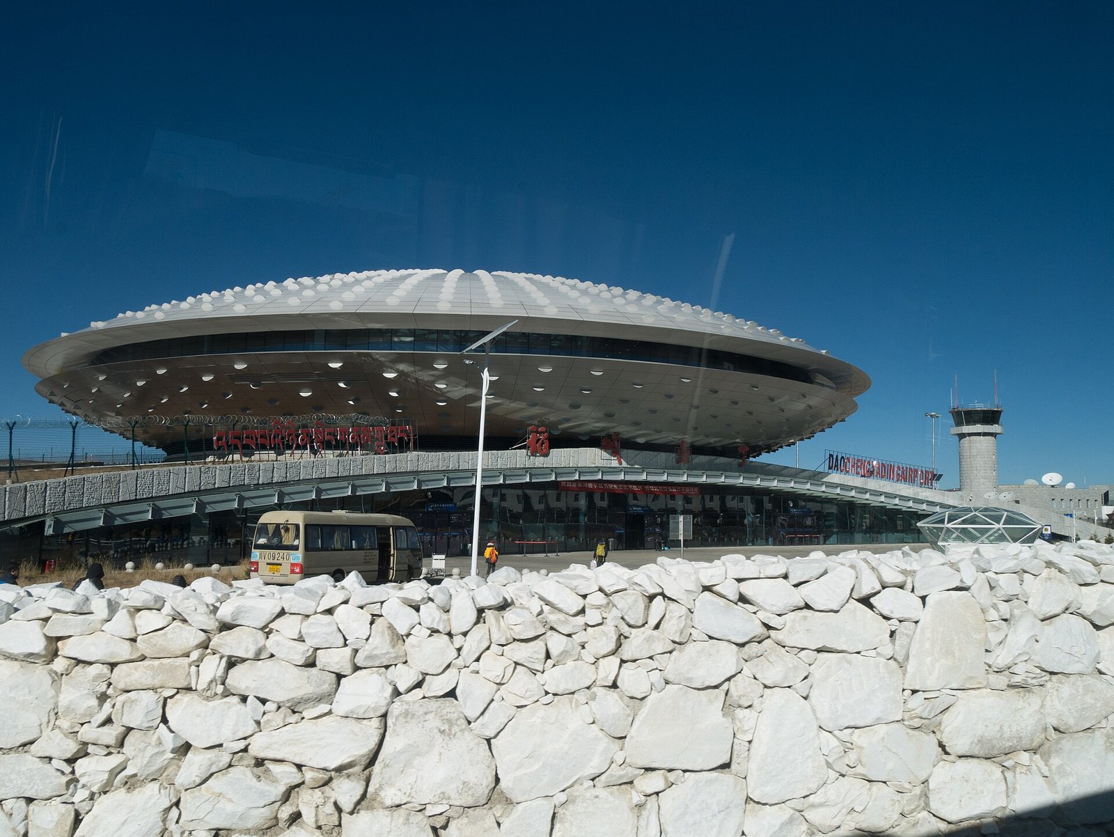 The low saucer-shaped terminal building of Daocheng Yading Airport on a stone plateau under a deep blue sky