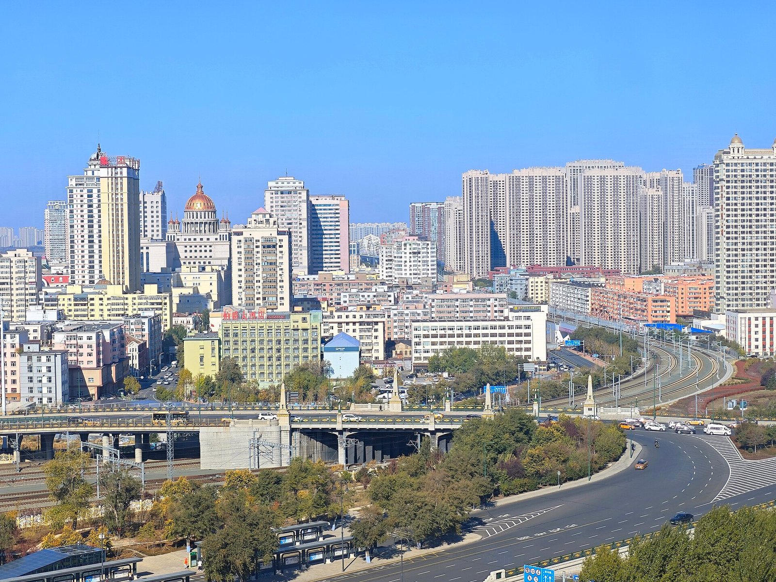 The Harbin skyline seen across the Songhua River, with modern towers rising behind an old steel bridge