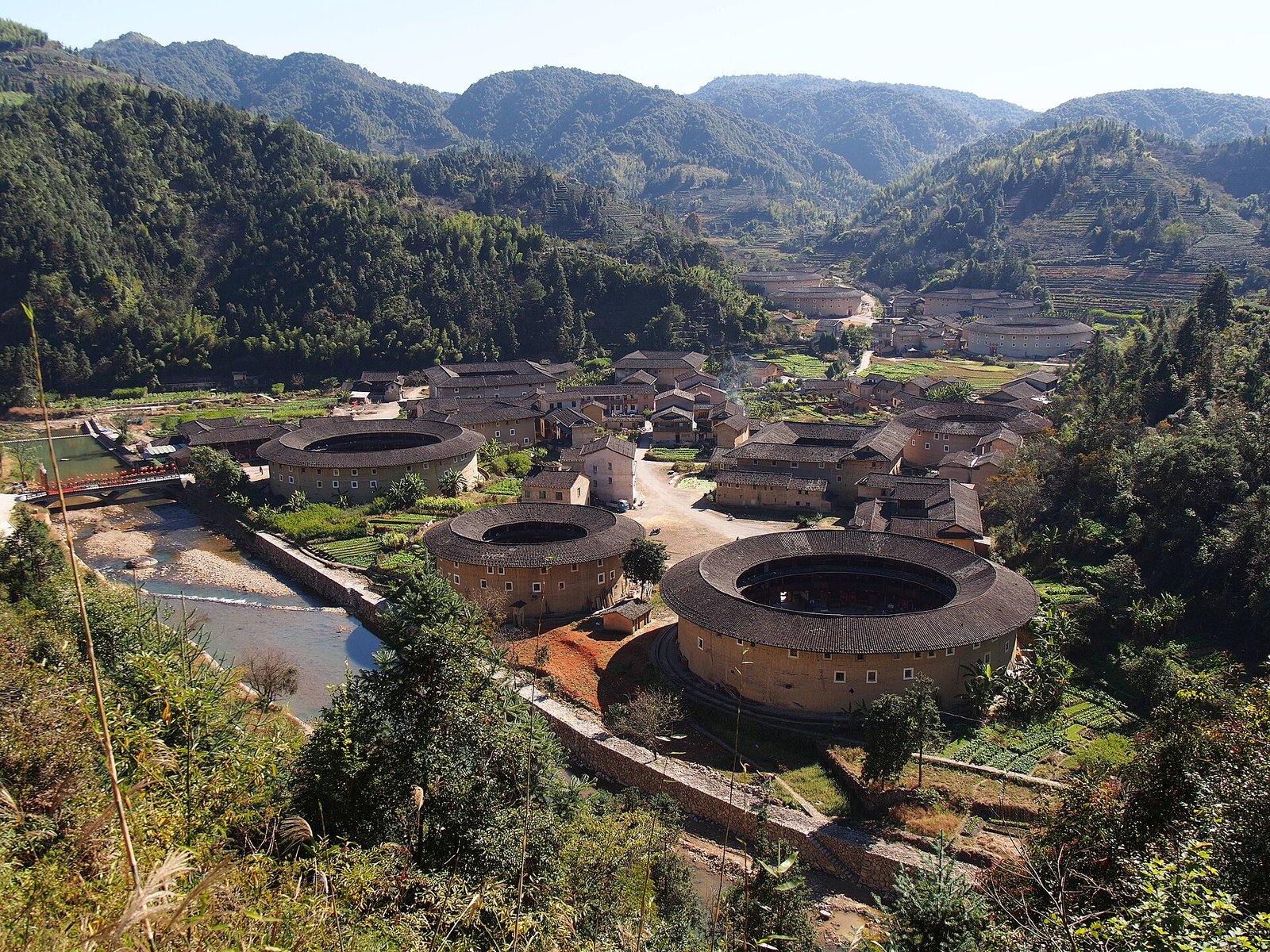 The Hekeng tulou cluster seen from the ridge above, with square and round earthen buildings spread across a narrow valley floor