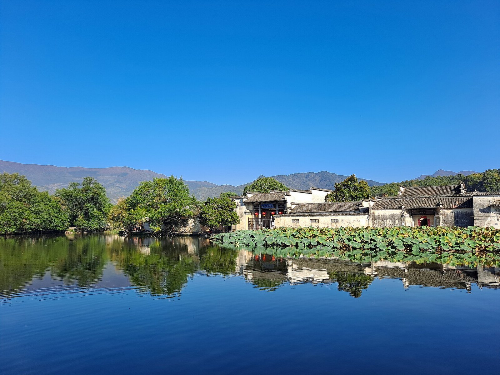 A wide lake reflecting the white-walled houses and trees of a Huizhou village