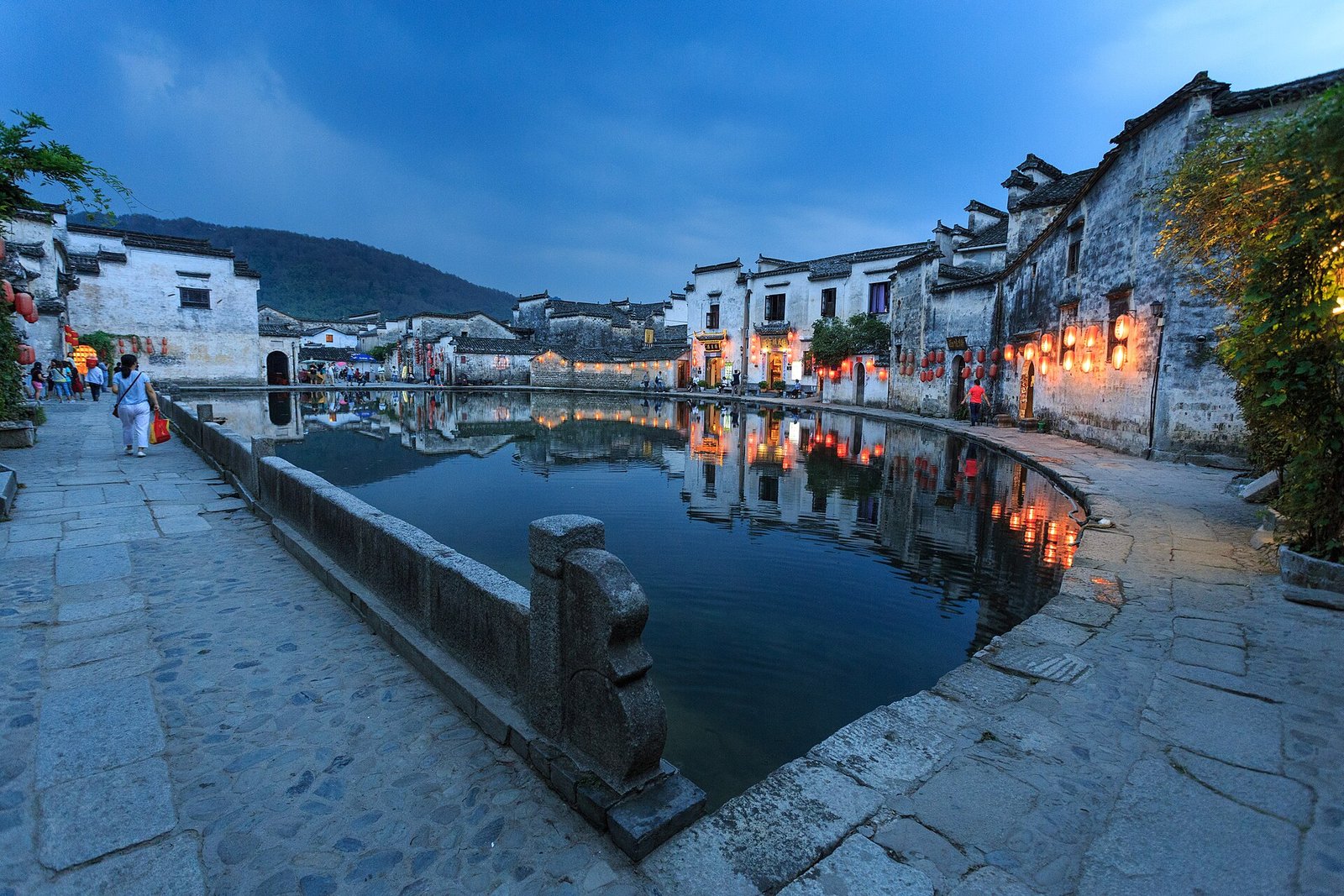 A Huizhou village of white walls and dark tiled roofs reflected in a still pond at dusk