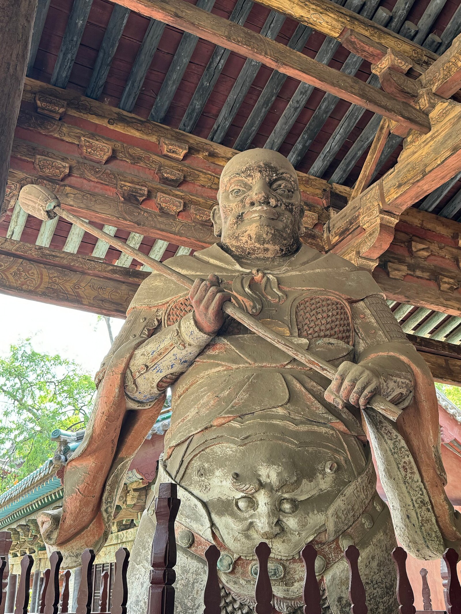 A painted clay figure of an armoured guardian seen from the side, with a weathered face and detailed armour