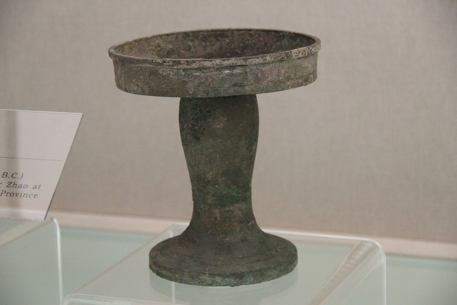 A bronze ritual vessel with a lid and a pedestal foot, lit against a dark museum background