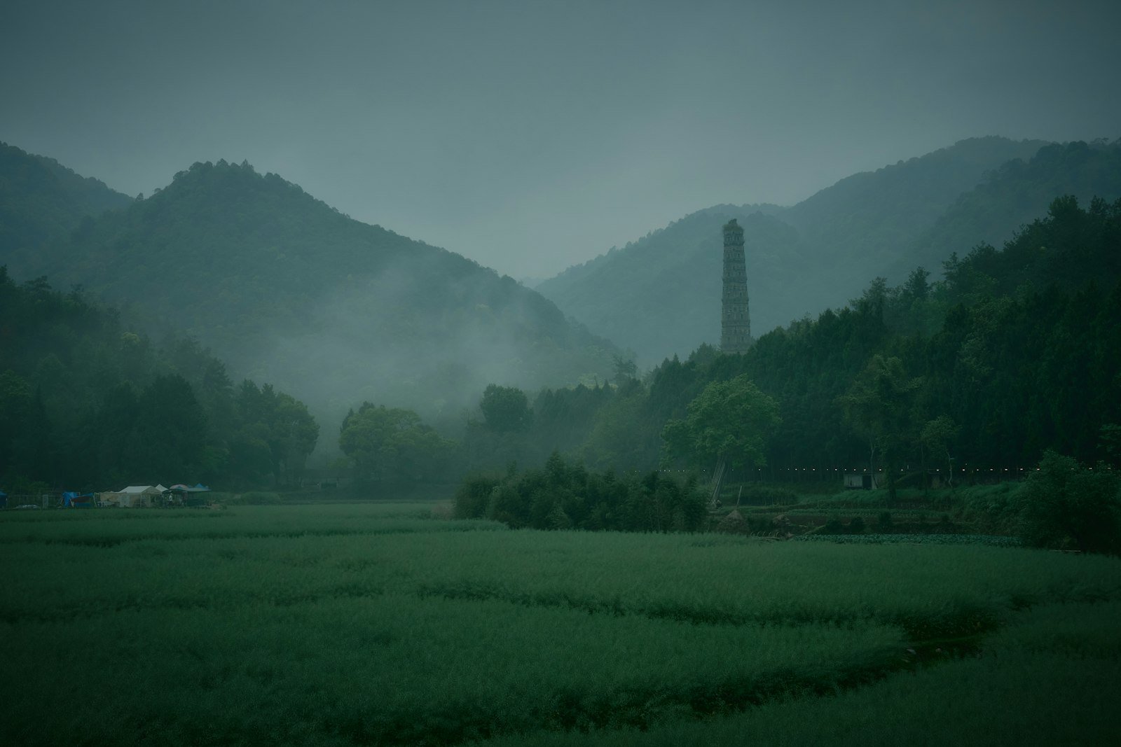 Green fields with a lone tower standing in the distance under a hazy sky