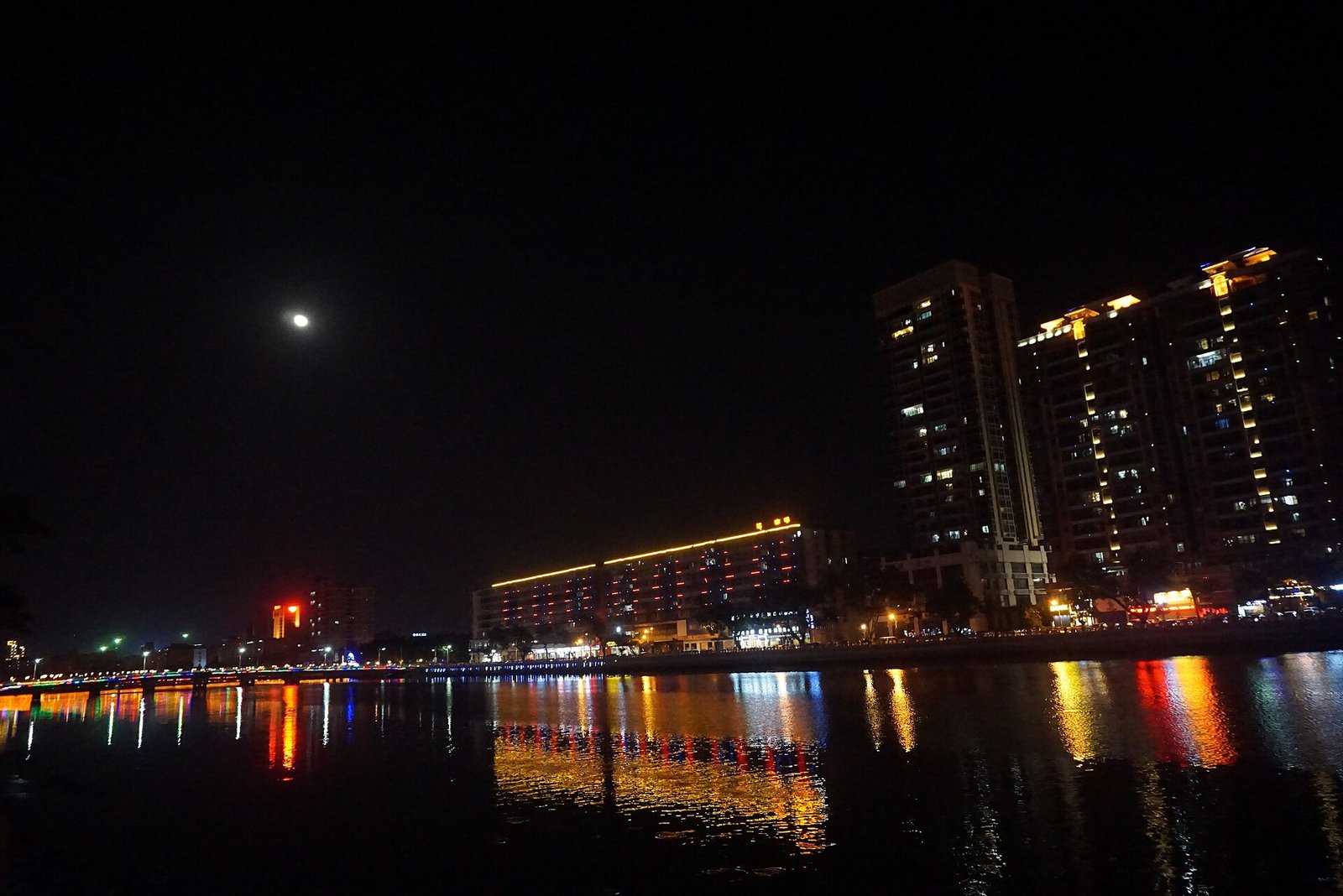 A river at night with lit buildings along the bank and a bridge reflected in the water