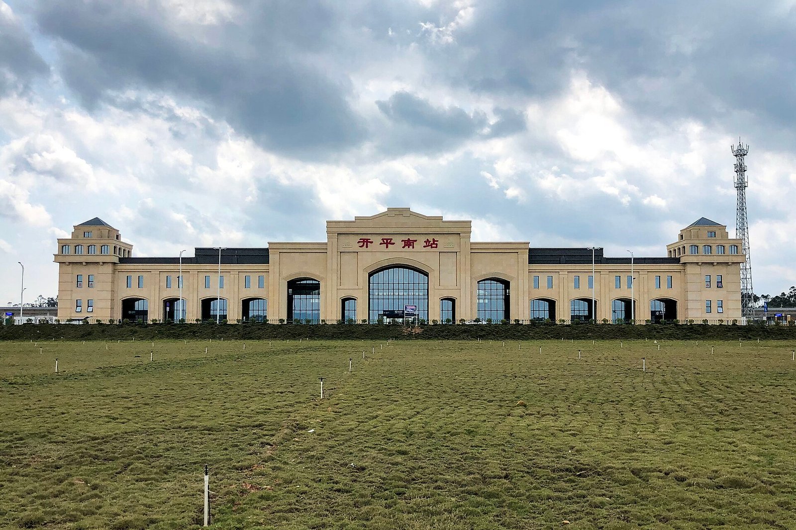 A long low station building in pale stone with two corner towers with pyramidal roofs and a tall central arch