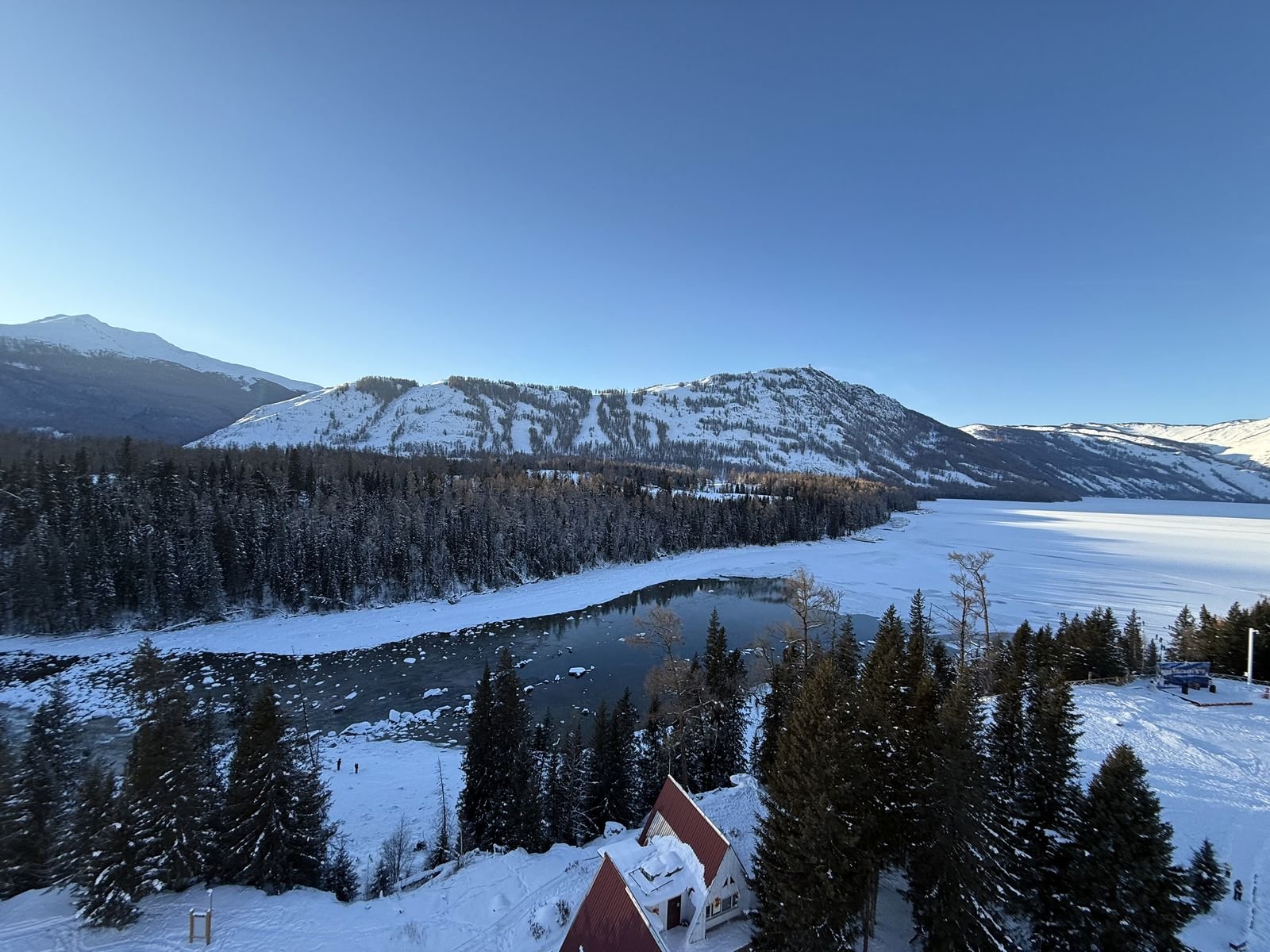 The frozen Kanas lake and river in winter, with a snow-covered forest and mountains beyond