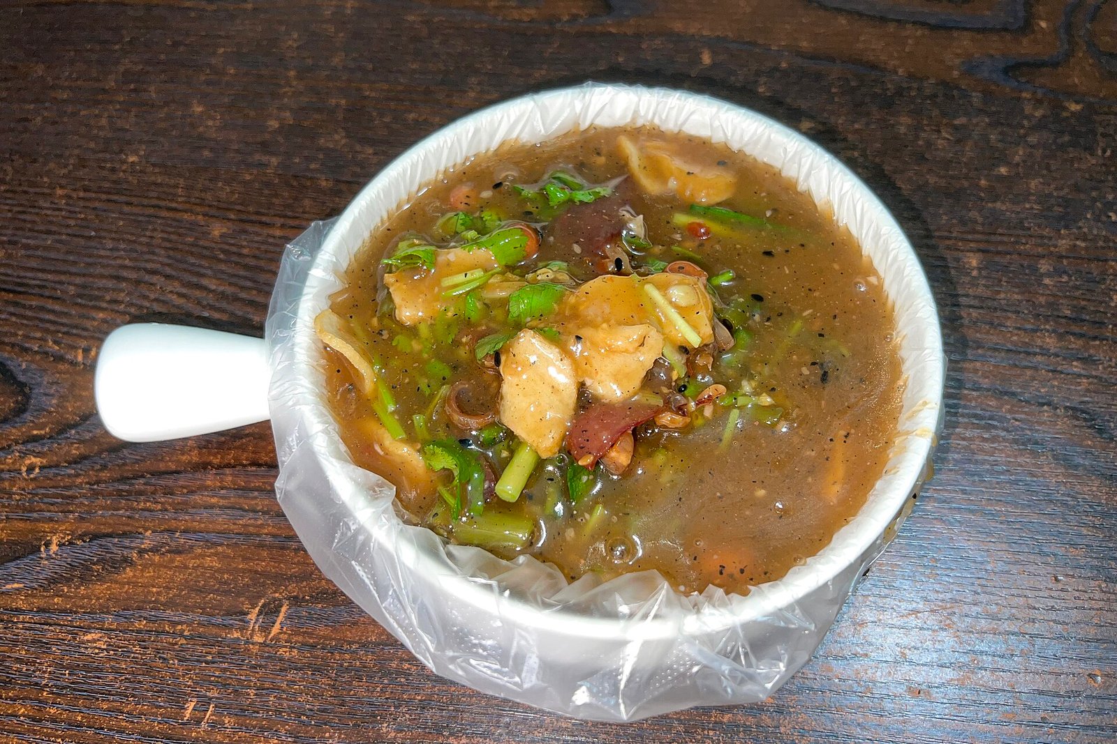 A bowl of Lingshui suanfen rice noodles with peanuts, herbs and sliced toppings in a dark broth