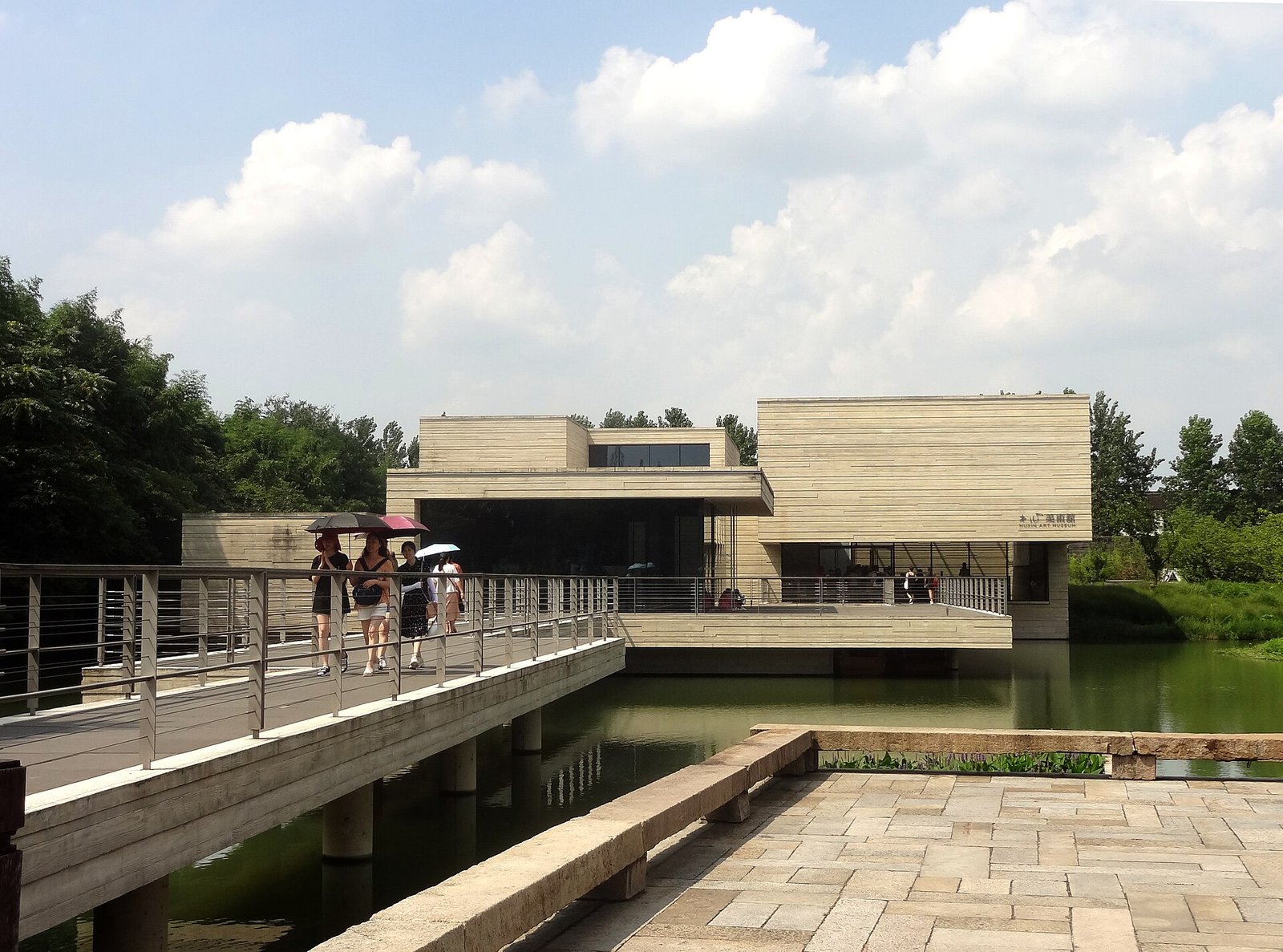The low concrete and glass Mu Xin Art Museum at Wuzhen, reflected in a shallow pool, with a pagoda visible behind