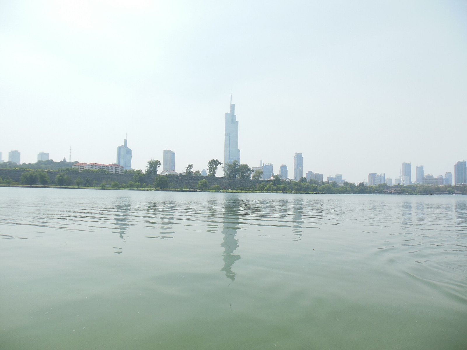 A modern Chinese city skyline seen across a calm lake at dusk