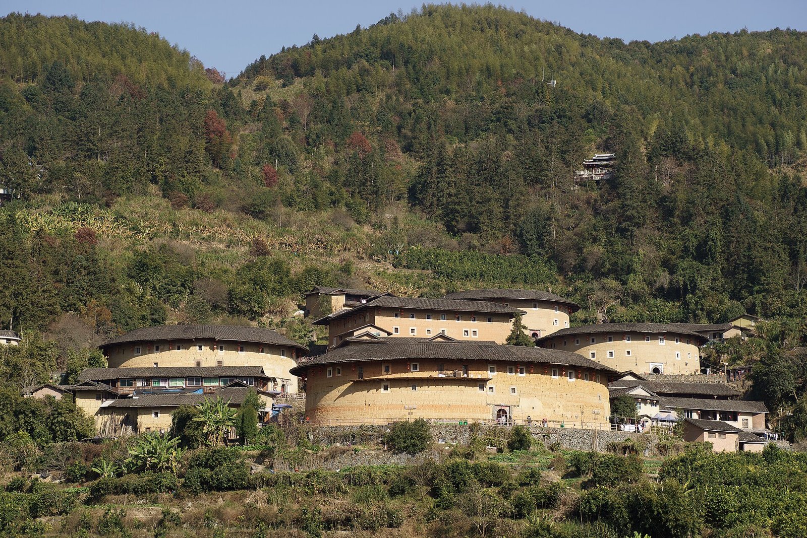 Earthen tulou buildings scattered across a forested valley floor in Nanjing County, Fujian, seen from a distance through haze