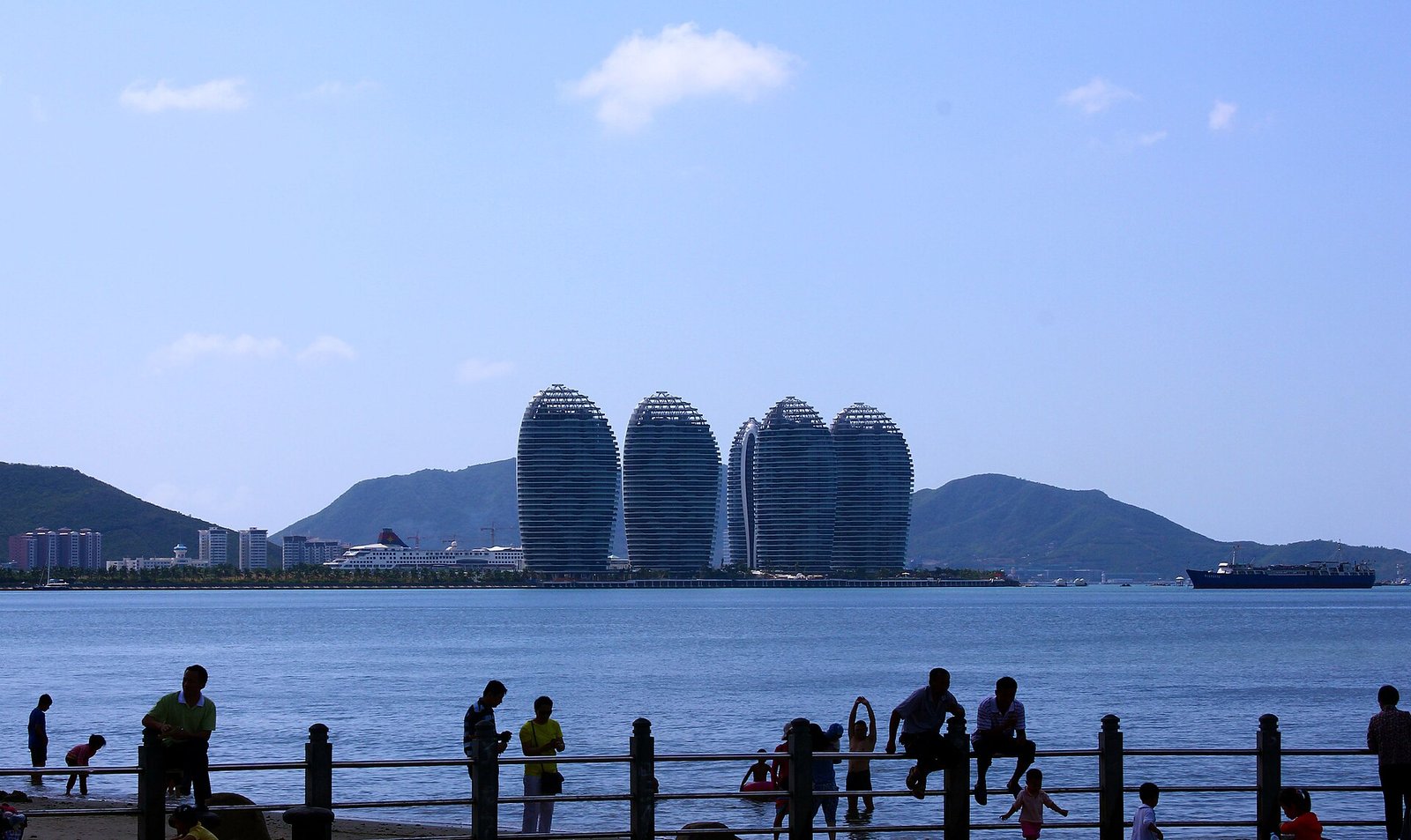The curved towers of Phoenix Island seen from a waterfront pier with people silhouetted against the water