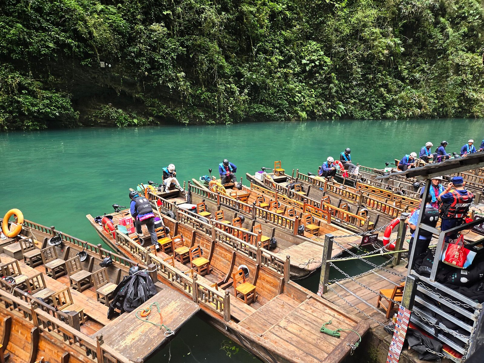 A shallow wooden boat carrying visitors on clear green water in Pingshan Canyon, Hefeng county, Hubei
