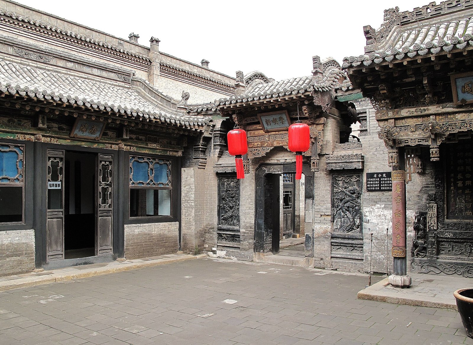 An ornate Chinese courtyard with wooden carvings, red lanterns and a stone-paved walkway