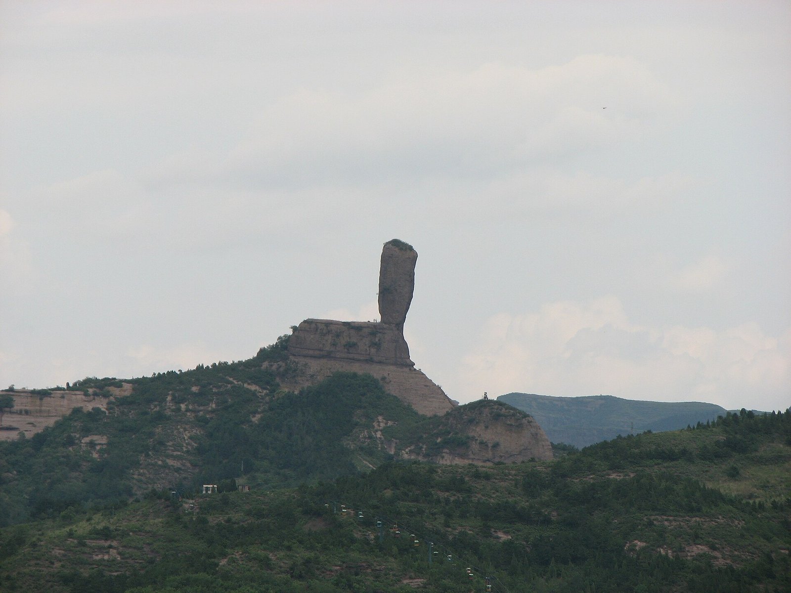 A tall granite rock column with a boulder balanced on top, standing on a ridge near Chengde