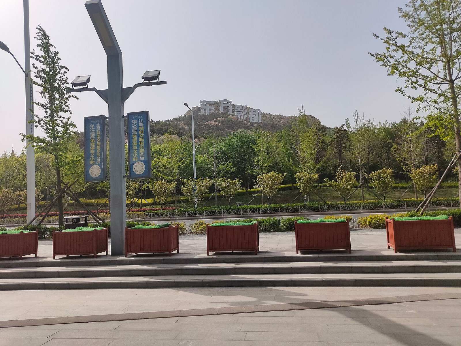 A wide empty road with signposts and low buildings, a green hill rising behind them under a clear sky