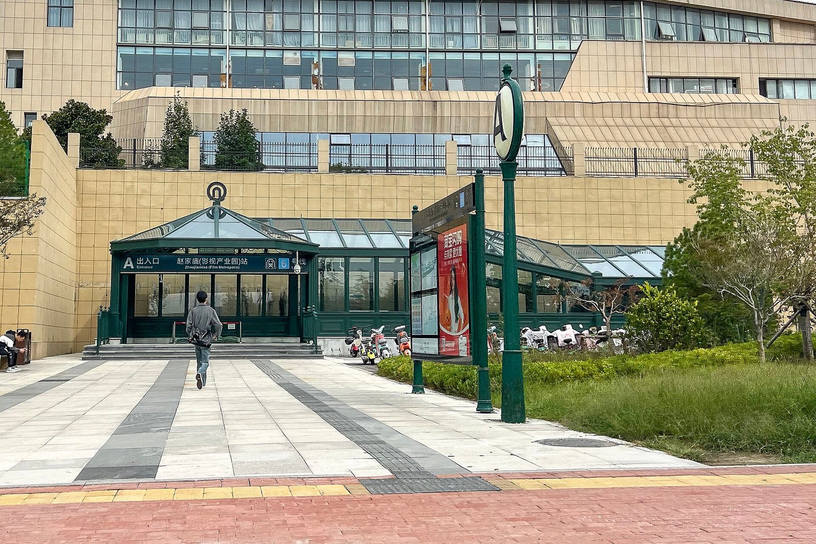 A glass and green-metal metro entrance canopy with a sign reading Zhaojiamiao (Film Industrial Park) Station, Exit A, on a wide paved forecourt