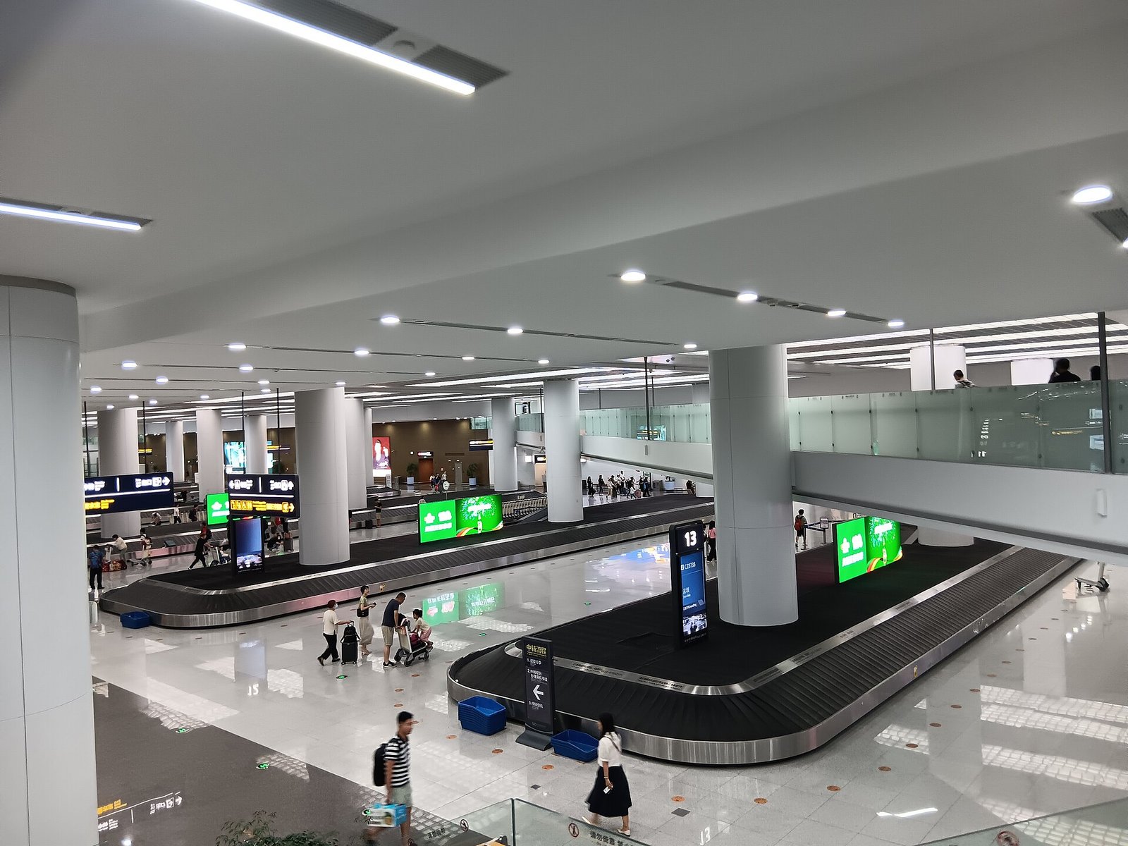 A modern airport baggage hall with stainless steel carousels, a curved ceiling and passengers waiting