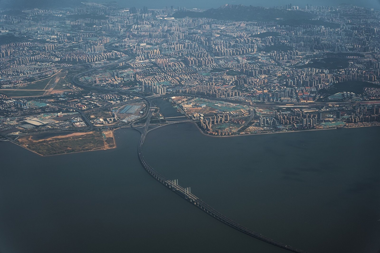A long sea bridge on slender piers curving across open water, seen from the air