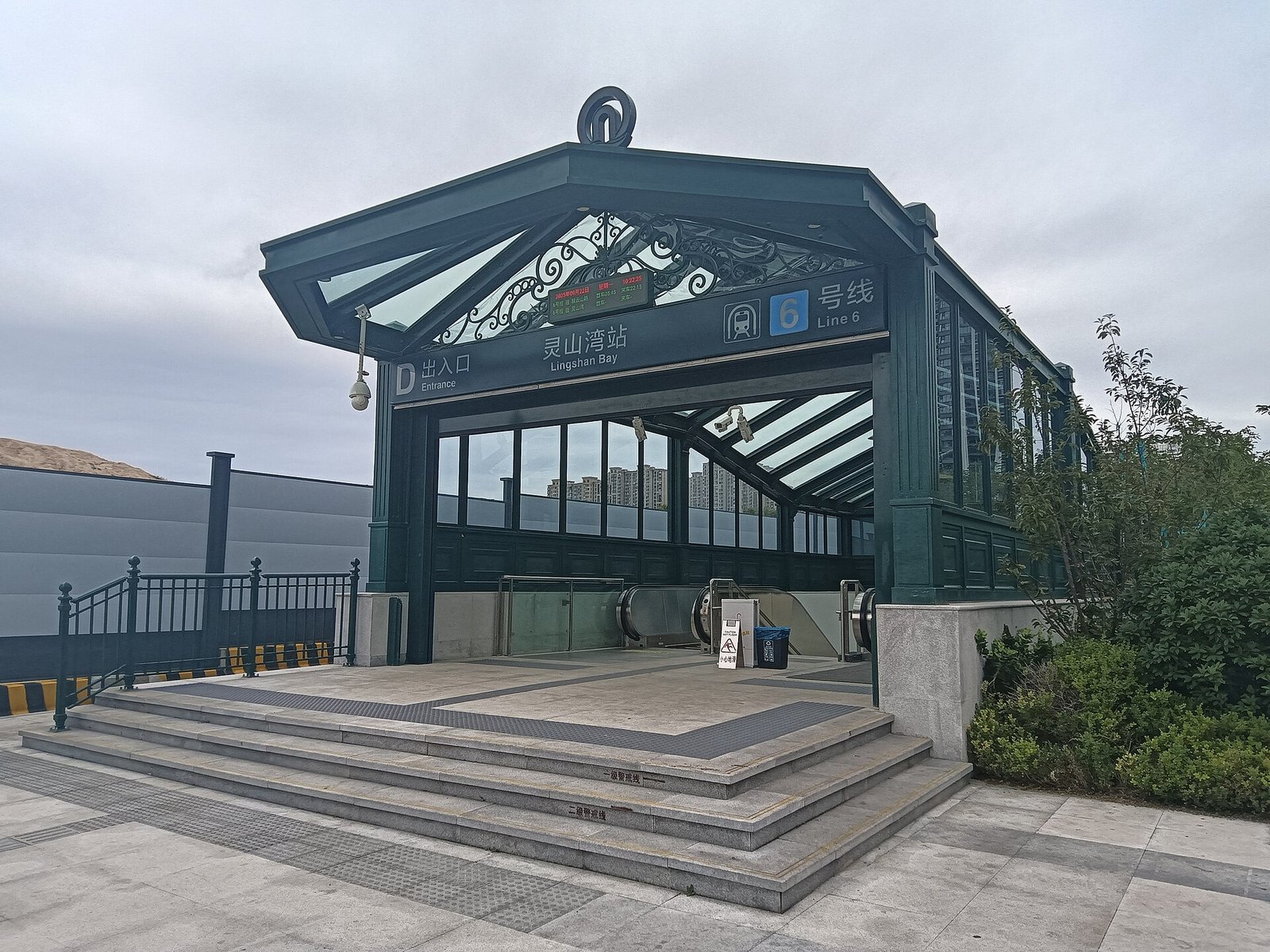 A metro station entrance with a dark green steel canopy, steps, and a paved approach