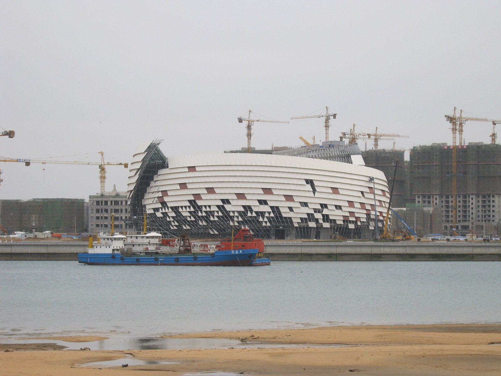 A white shell-shaped theatre building with a patterned glass facade, seen across a wide empty plaza