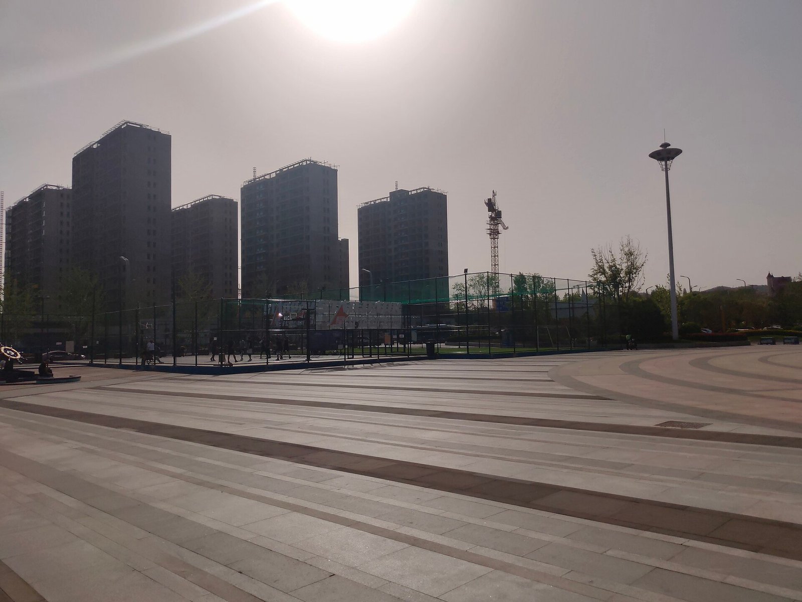 A running track and sports ground with apartment blocks and a hill behind, under a bright sky