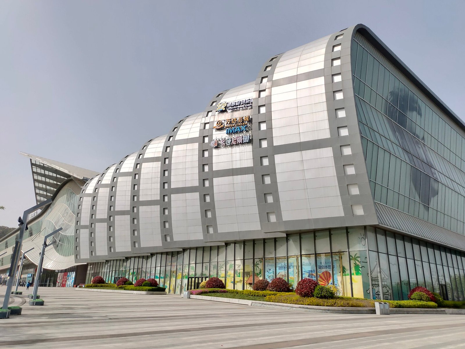 A large modern shopping centre with dark glass and pale stone cladding, and a cylindrical glass entrance