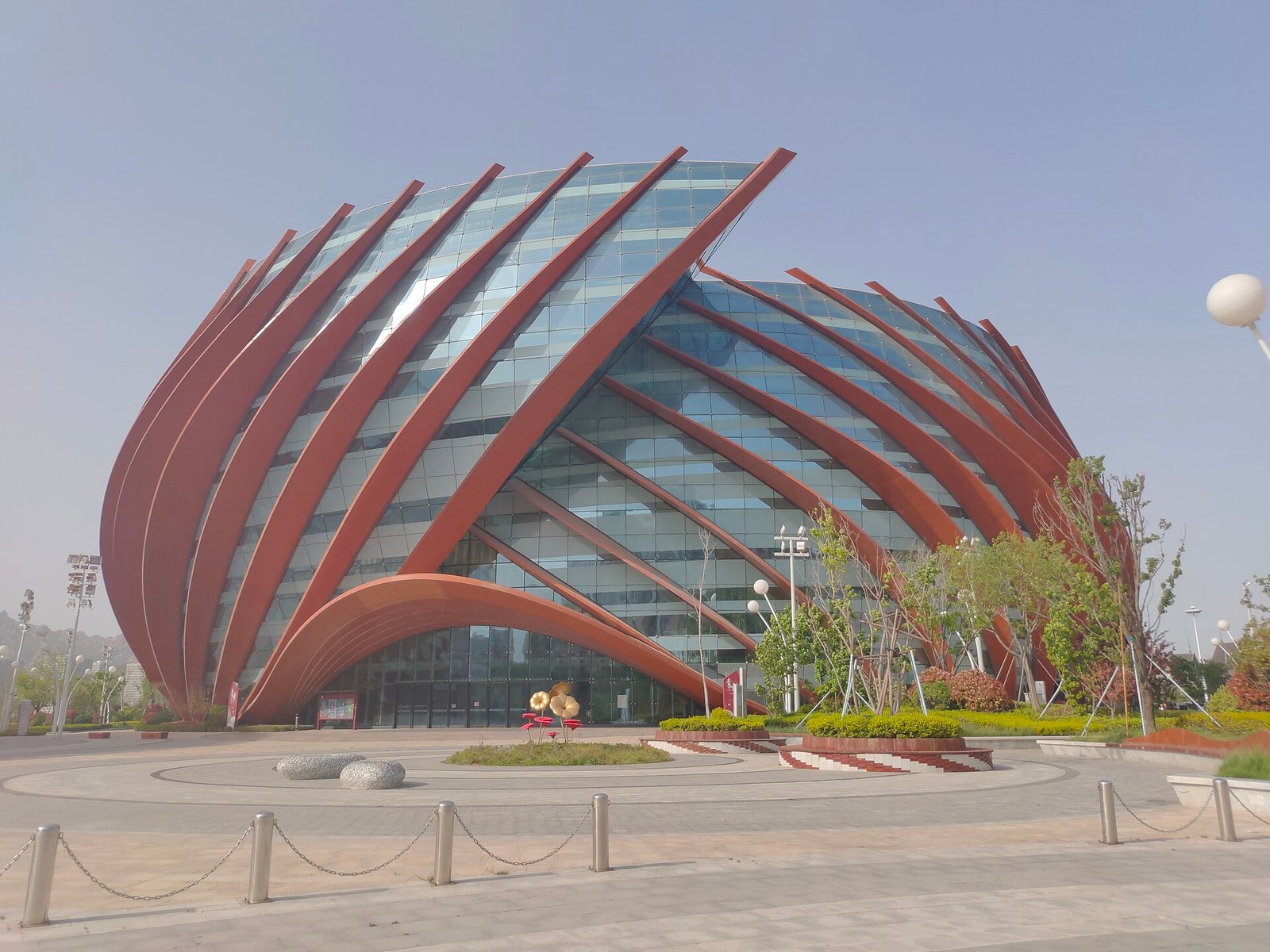 A tall orange-red lattice structure shaped like an opening shell, standing against a clear sky
