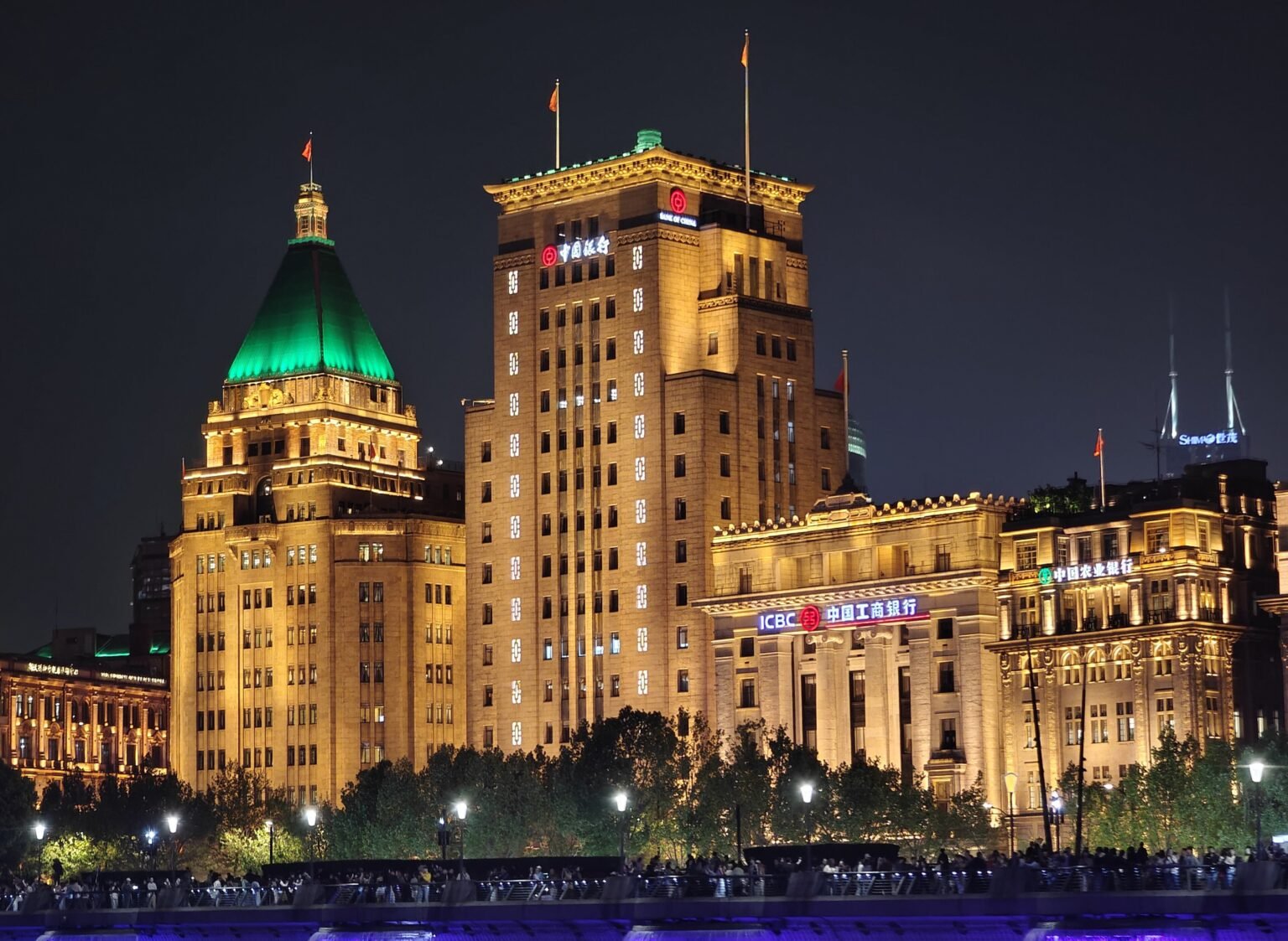 The historic Bund waterfront in Shanghai lit up at night, with the Peace Hotel's green pyramid roof on the left