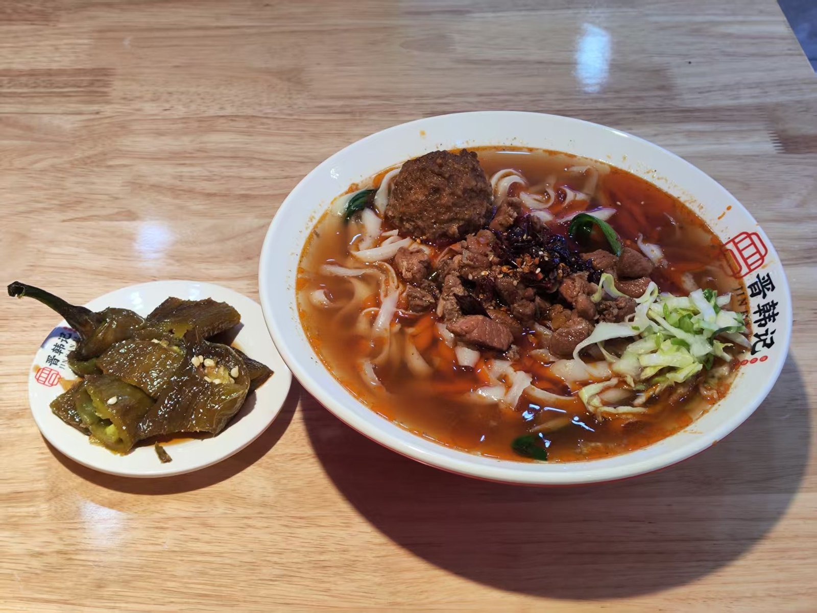 A bowl of thick irregular noodles in a dark sauce with greens, chopsticks resting on the rim