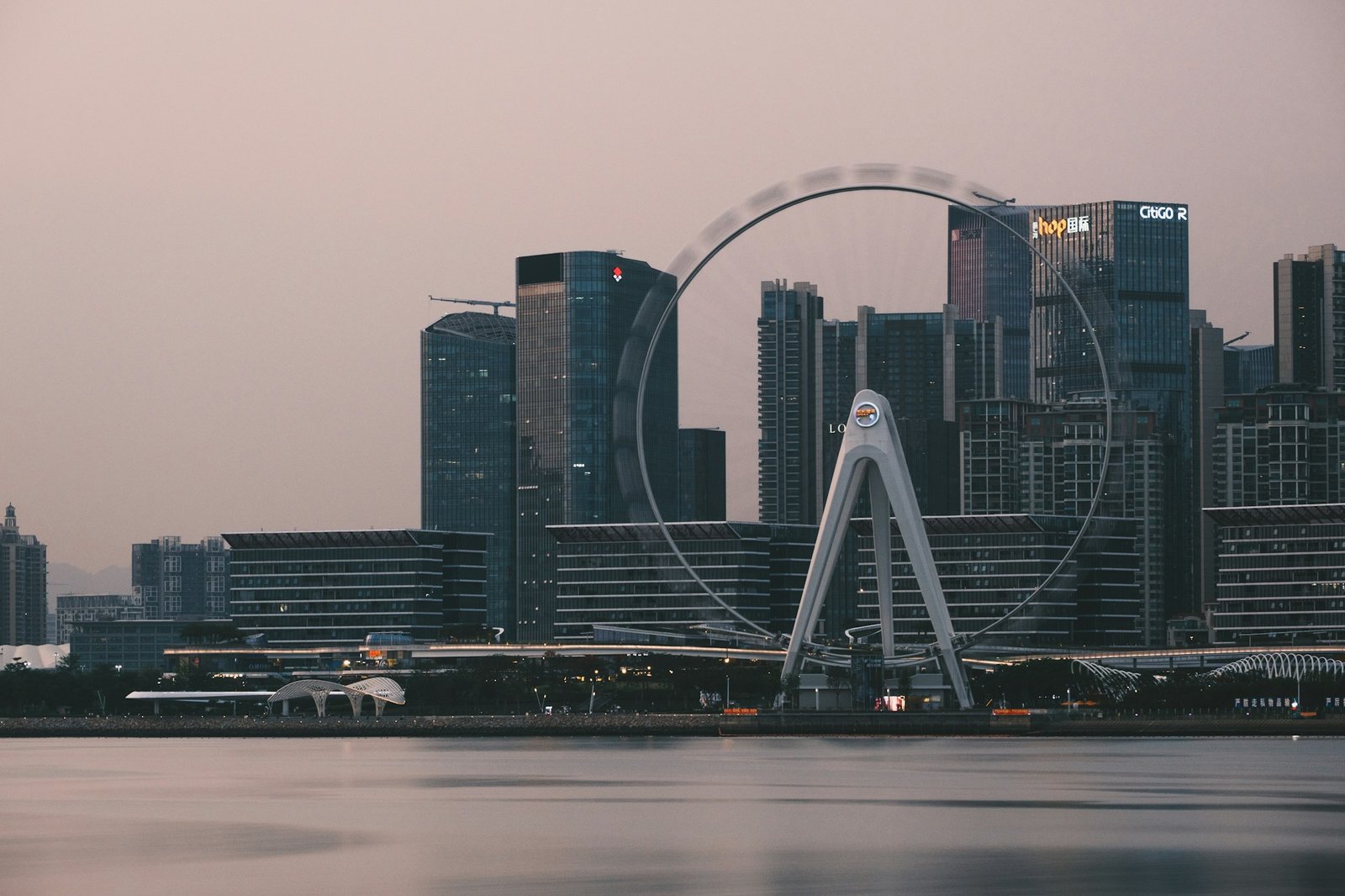 The Bay Area Light ferris wheel at OH Bay at dusk, turning in front of the Shenzhen towers