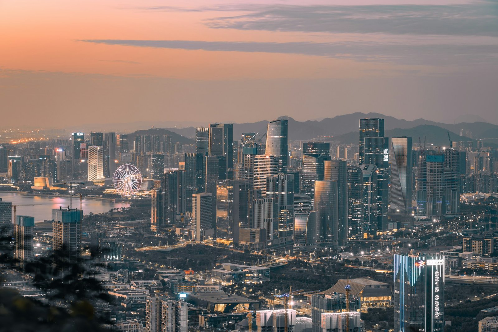 The Qianhai skyline at dusk with a ferris wheel glowing on the waterfront beyond the towers